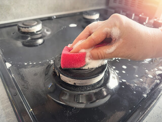 woman cleaning  sponge rag with white foam and detergent washing kitchen gas stove