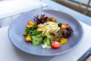 Delicious salad with squid, boiled potatoes and fresh vegetables, served with olive oil