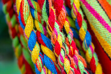 Colorful cotton rope. Thick cotton rope showing detail of threads and fibres. Yarn braid rope of cradle. Multicolored yarn has been braided into a braid. Knitted fabric background. Selective focus.