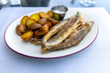 Fried smelt with boiled potatoes and mushroom sauce on a white plate. Delicious rustic lunch