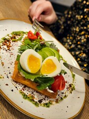 Delicious Belgian waffles with egg, with microgreens, avocado and vegetables in a plate, close-up. Delicious sandwich with egg. Ketogenic diet breakfast