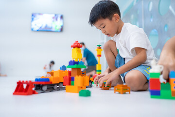Happy kindergarten asian boy enjoying play colorful toy train block on white lession room