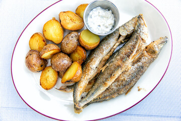Fried smelt with boiled potatoes and mushroom sauce on a white plate. Delicious rustic lunch
