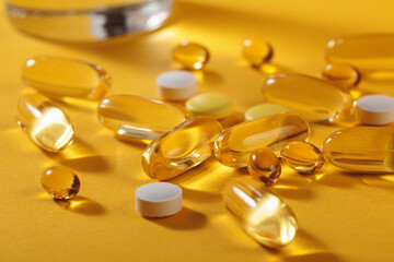 Diet, nutrition, healthy eating concept. Assorted Oil filled yellow softgels capsules and pills of food supplements and glass of water for pouring on yellow background