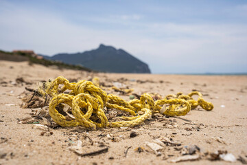 Yellow rope lying on a sandy beach with mountain in the background. Environmental pollution and...