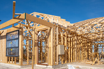 A suburban house under construction with wooden beams and timber studs, forming the frame of a...