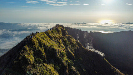 Climbers walk volcano crater rim during cloud inversion sunrise. Mt Batur, Bali. 