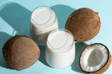 Coconut milk in a glasses among coconuts on a blue background