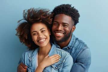 Portrait of a happy mixed race couple in their 30s sporting a versatile denim shirt while standing against soft blue background