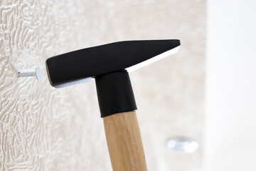 hammer drives nail into white wall at home