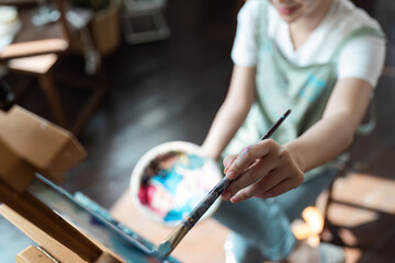 Close-up of a Person Engaged in Painting as a Creative Hobby, Holding a Brush and Palette, in a Cozy and Artistic Home Studio Setting