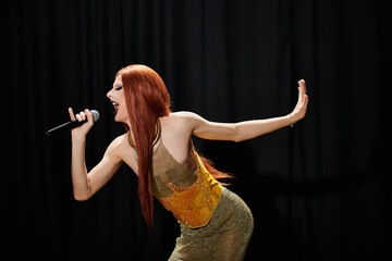 A drag queen performs on stage, microphone in hand, showcasing her bold fashion.