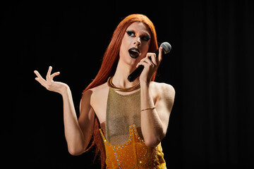 A drag queen with long red hair performs on stage, holding a microphone.