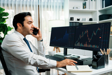 Trader businessman calling to consultant or partner with two stock exchange investment, compare...