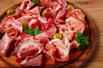 Assortment , sliced meat appetizer, prosciutto, salami and ham, with olives, on a wooden board, breakfast, top view, close-up, no people,