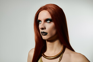 A drag queen poses for a portrait, showcasing a bold makeup look and flowing red hair.