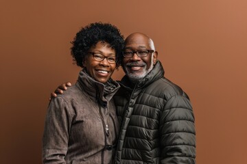 Obraz premium Portrait of a glad afro-american couple in their 40s donning a durable down jacket in front of soft brown background