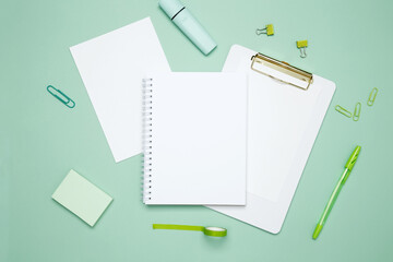 Creative flat lay mockup design of workspace. Top view composition with white notebook, to do list and stationery on green background
