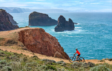 happy active senior woman cycling on the the rocky cliffs of the Vicentina coast of  Algarve,...