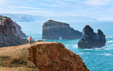 happy active senior woman cycling on the the rocky cliffs of the Vicentina coast of  Algarve,...