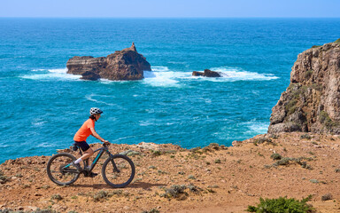 Fototapeta premium happy active senior woman cycling on the the rocky cliffs of the Vicentina coast of Algarve, Portugal near Sagres and Vila do Bispo 