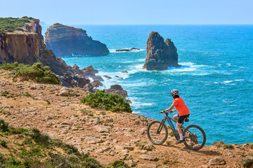 happy active senior woman cycling on the the rocky cliffs of the Vicentina coast of  Algarve,...