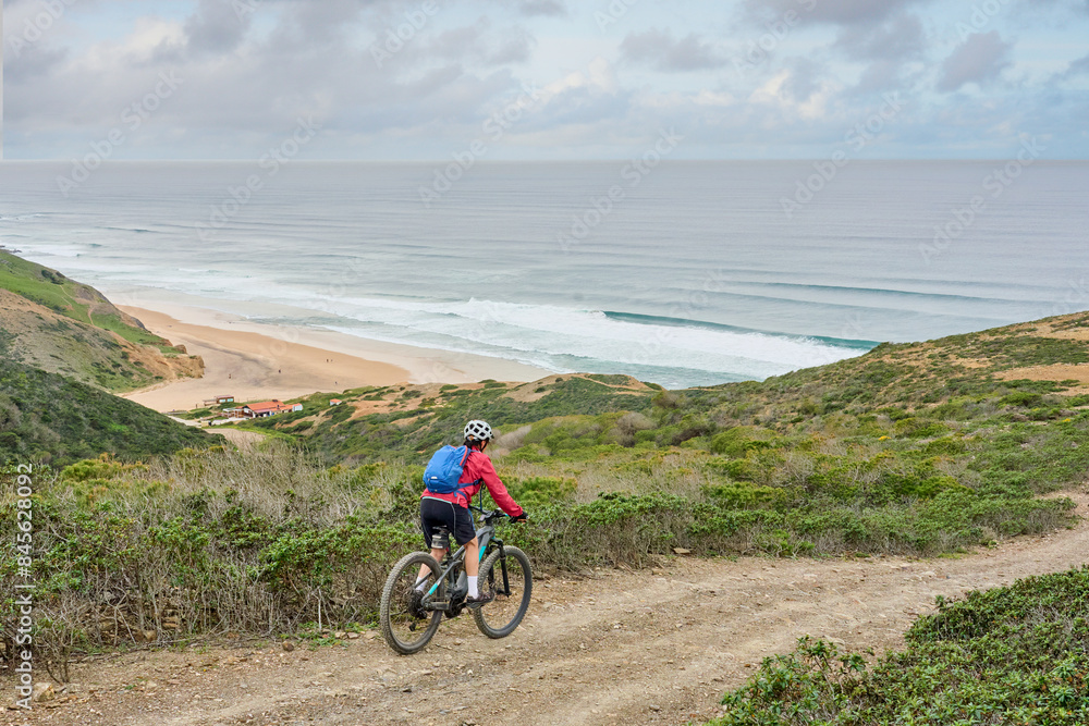 Wall mural happy active senior woman cycling on the the rocky cliffs of the Vicentina coast of  Algarve, Portugal near Sagres and Vila do Bispo 