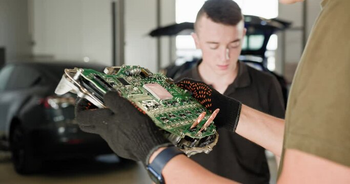 Two mechanics closely inspecting the circuit board of an electric car engine during repair and maintenance in a workshop. Work on advanced automotive technology. EV repair and service concept.