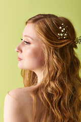 A young woman in white attire, with floral accents in her hair, looks off into the distance on her...