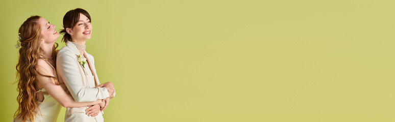 Two brides in white wedding attire embrace on a green background, celebrating their love.