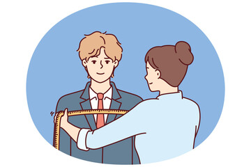 Woman tailor measures shoulders of man in centimeters to make formal suit to individual measurements. Guy at reception at tailor making handmade clothes according to individual sketches