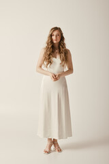 Fototapeta premium A beautiful young bride stands in a simple white wedding dress on a white background.