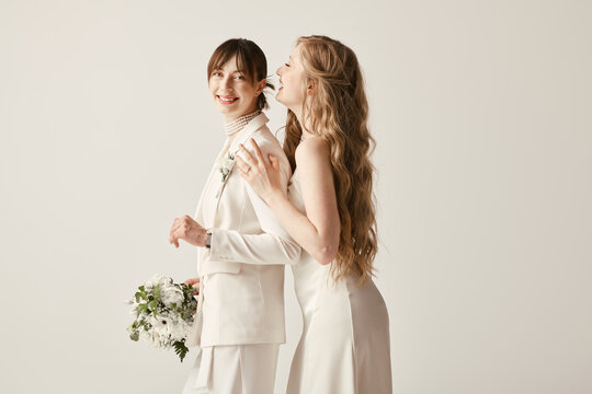 Two brides, dressed in white, stand close to each other during their wedding ceremony.