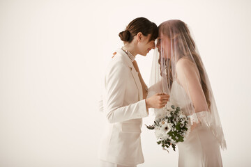 A lesbian couple in white wedding attire share a sweet moment during their wedding ceremony.
