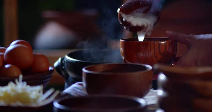 A porridge shop at night on the side of the road as the cook uses a wooden ladle to scoop porridge into a wooden bowl in a retro style. There were eggs and sliced ​​ginger placed on the table.