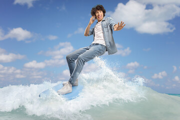 Man in jeans surfing on a surfboard and using a smartphone