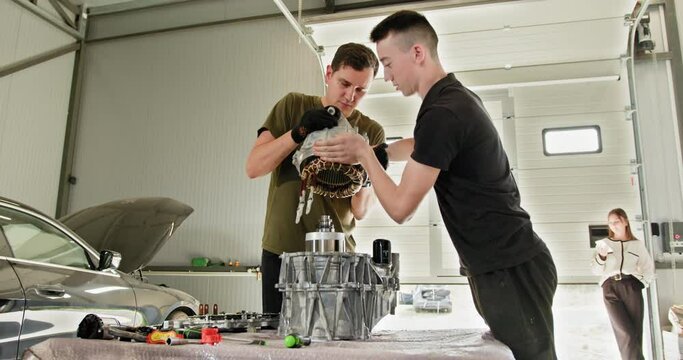 Two mechanics working diligently on an electric car engine inside a modern repair shop. Focused on engine maintenance and repair of an electric vehicle. EV repair and service concept.