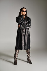 Naklejka premium A plus size woman exudes confidence in a stylish black leather coat and boots against a gray backdrop.