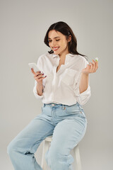 A plus-size woman in stylish attire engrossed in using a cellphone while sitting on a stool against...