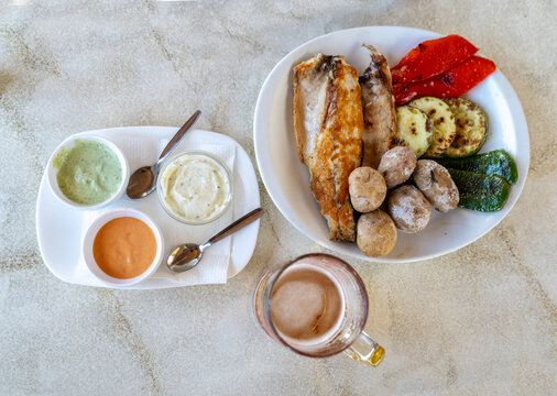 Papas arrugadas, grilled fish, grilled vegetables, red mojo, green mojo, beer mug. Traditional Canarian food