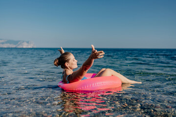 A woman is floating in a pink inflatable raft on a calm ocean