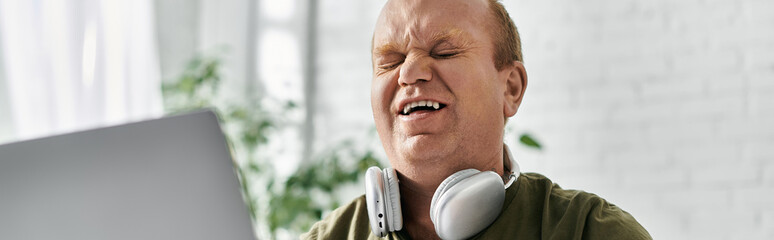 A man with inclusivity is singing along to music while wearing headphones at home.