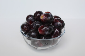Dark purple or black grapes, off the stem, or without stalk, inside transparent bowl, isolated on white background