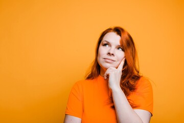 Portrait of young thoughtful dreamy girl, bright orange background
