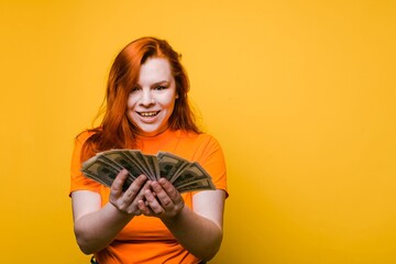 Portrait of a happy young woman holding banknotes, bright yellow background, copy space