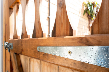 Shallow focus of a newly installed, hardwood ornate side gate, focusing on the large metal door hinge brackets and screws. See after a summer downpour.