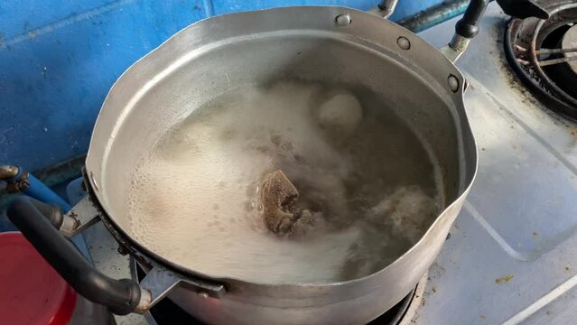Boiling bone broth soup in pot at gas stove at kitchen at home point of view shot