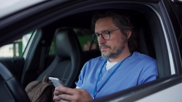 Doctor in car, going home from work, scrolling phone. Work-life balance of healthcare worker.