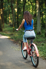 Naklejka premium Close up rear view of beautiful woman on bicycle in green summer park