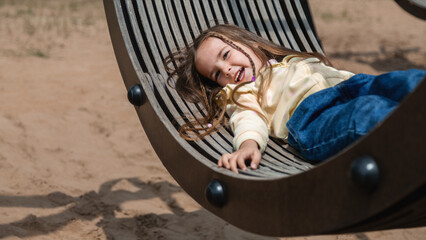 Little girl child rides on a swing. Adorable child resting while lying on a swing in the park